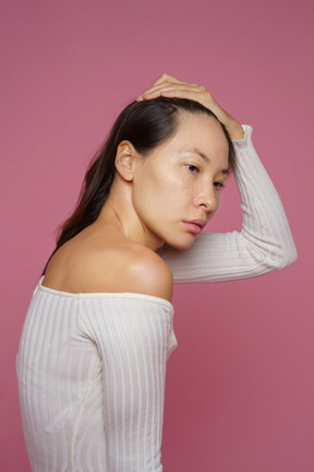 Three-quarter view of a sad dark-haired female touching her hair and looking aside