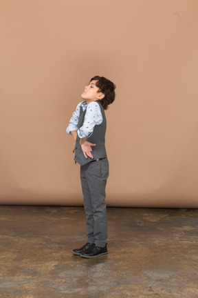 Vista lateral de un chico lindo en traje de pie con las manos en las caderas