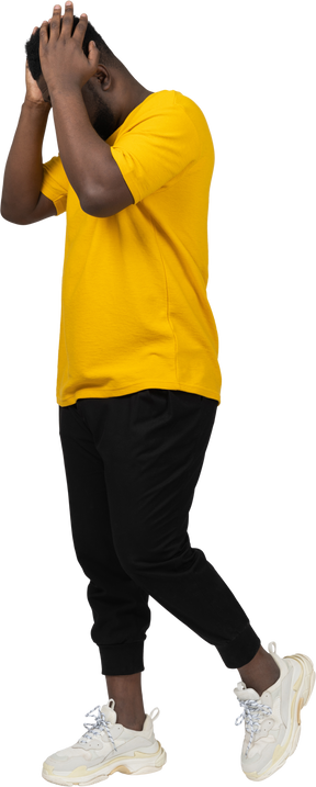 Side view of a walking young dark-skinned man in yellow t-shirt touching head