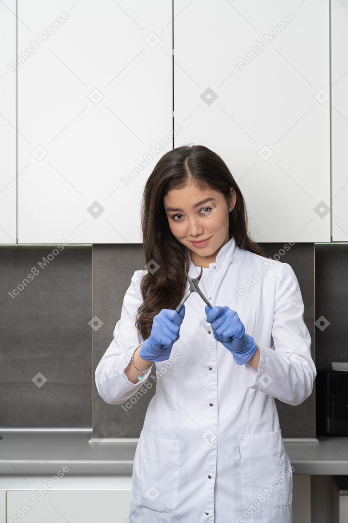Front view of a smiling female doctor looking at camera and holding dental instrument