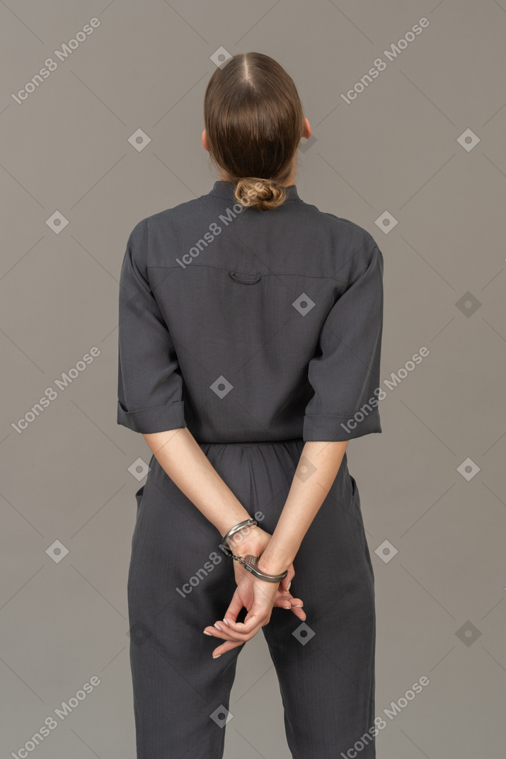 Вид сзади молодой женщины в комбинезоне в наручниках