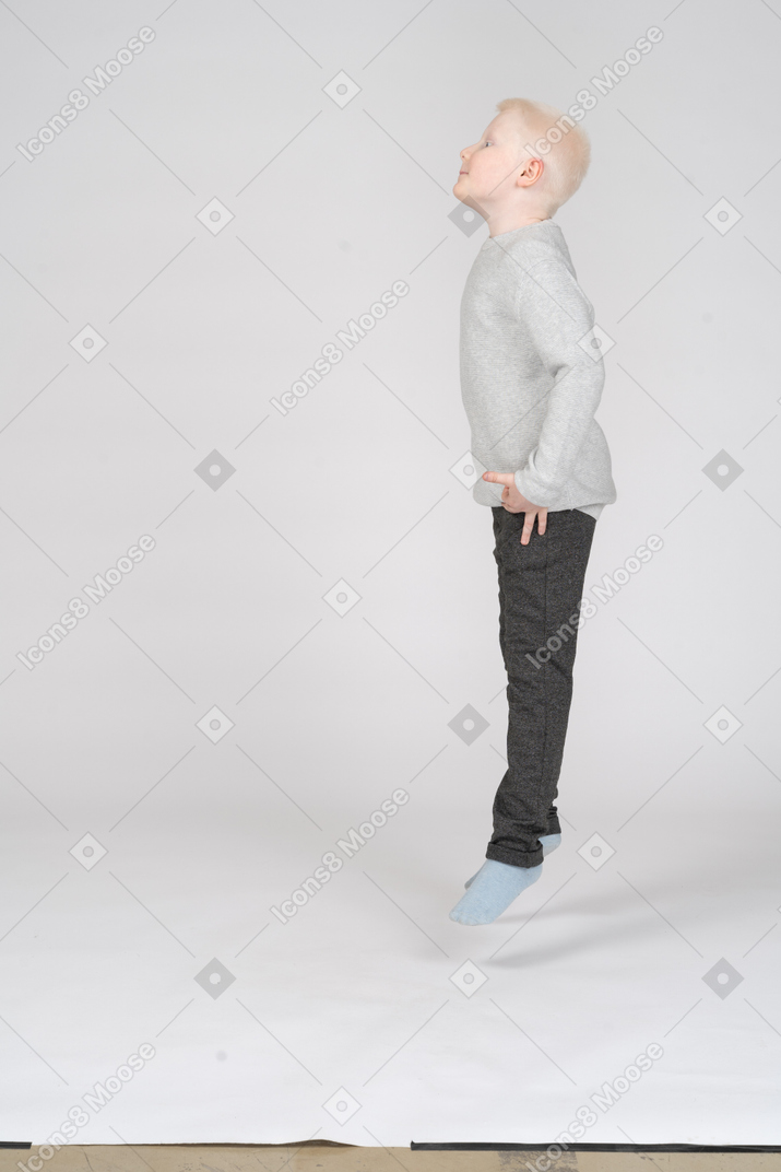 Vista lateral de un niño saltando y mirando hacia arriba