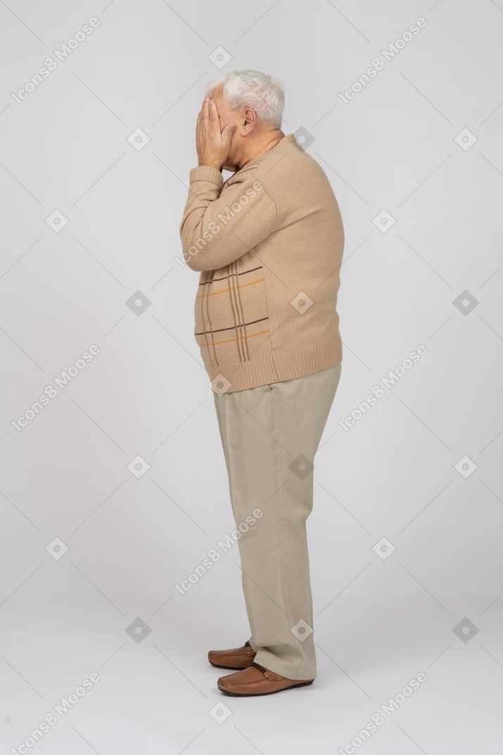 Вид сбоку на старика в повседневной одежде, закрывающего лицо руками