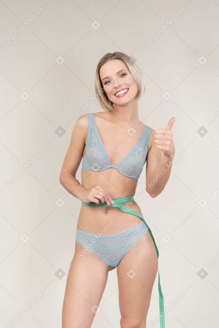 Jeune femme en lingerie mesurant sa taille et montrant le pouce vers le haut