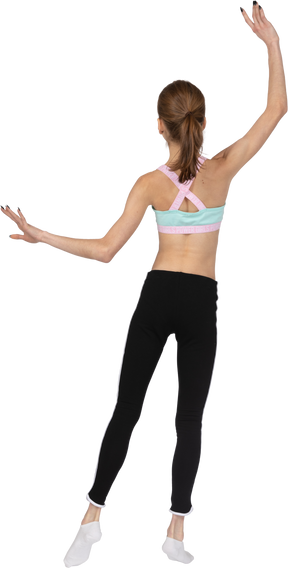 Vista posterior de una jovencita en ropa deportiva levantando las manos y poniendo su pierna a un lado