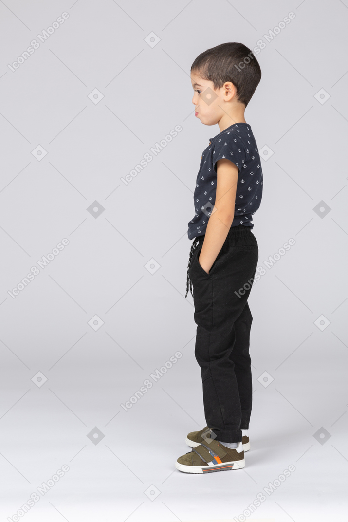 Vista lateral de um menino bonito posando com as mãos nos bolsos