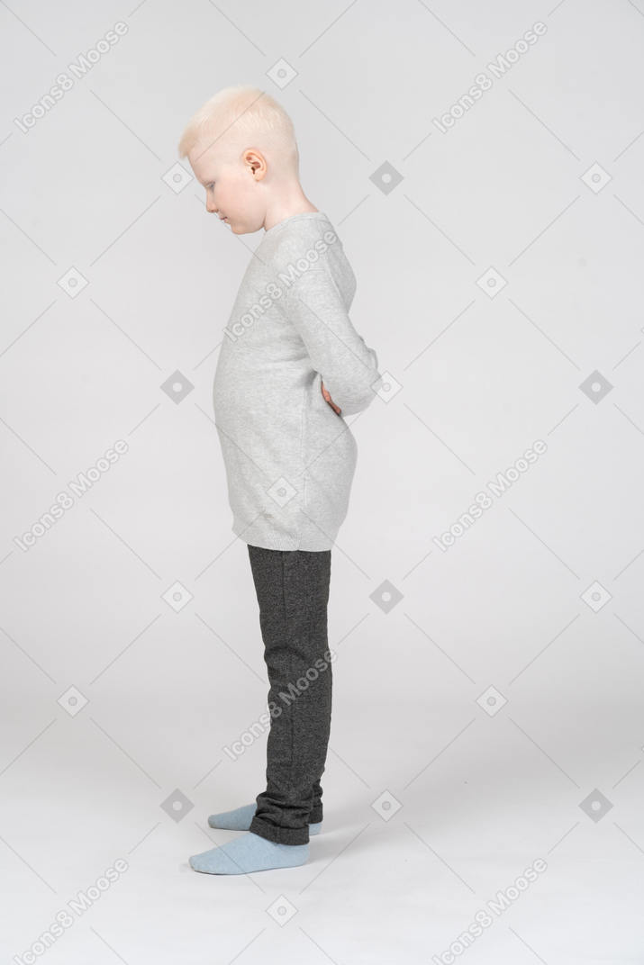 Un ragazzino biondo in abiti casual in piedi e nascondendo le mani dietro