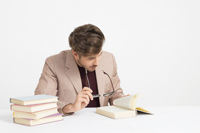 Apuesto joven sosteniendo sus gafas y leyendo un libro