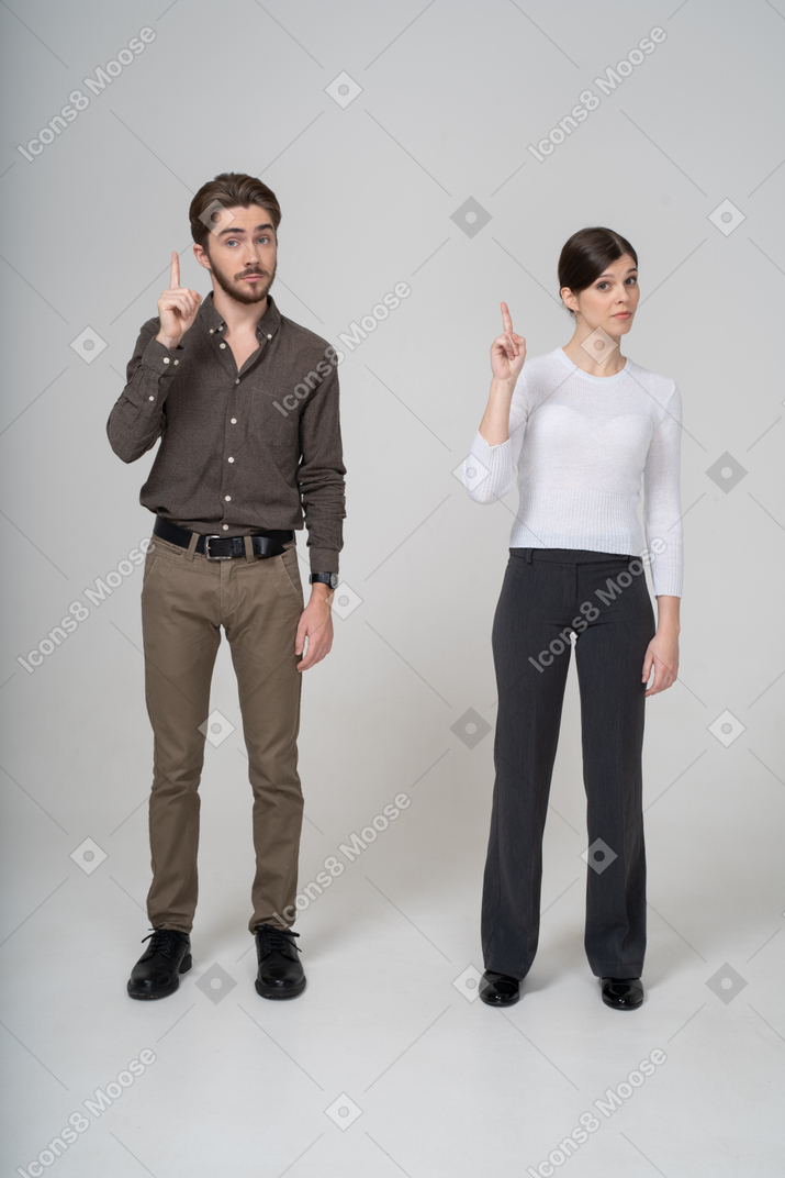 一对年轻夫妇在办公室服装举起手指的前视图