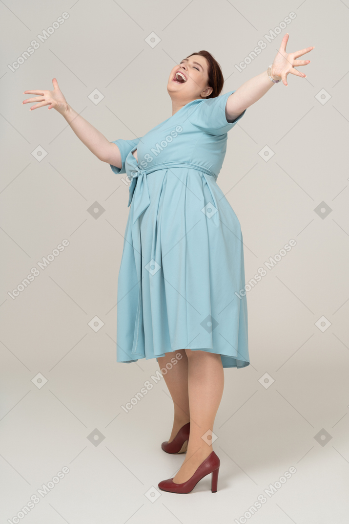 Вид спереди счастливой женщины в синем платье, позирующей с поднятыми руками