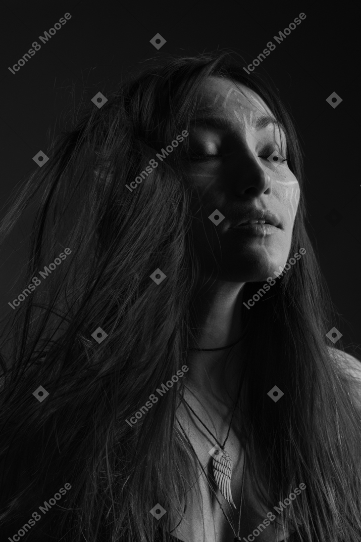 Noir three-quarter portrait of a young female with ethnic facial art and messy hair closing her eyes