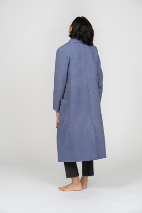 Vista traseira de uma mulher com um casaco em pé com os braços nas laterais