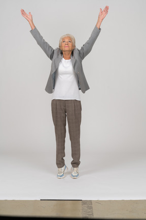 Vista frontal de uma senhora idosa de terno na ponta dos pés e levantando os braços
