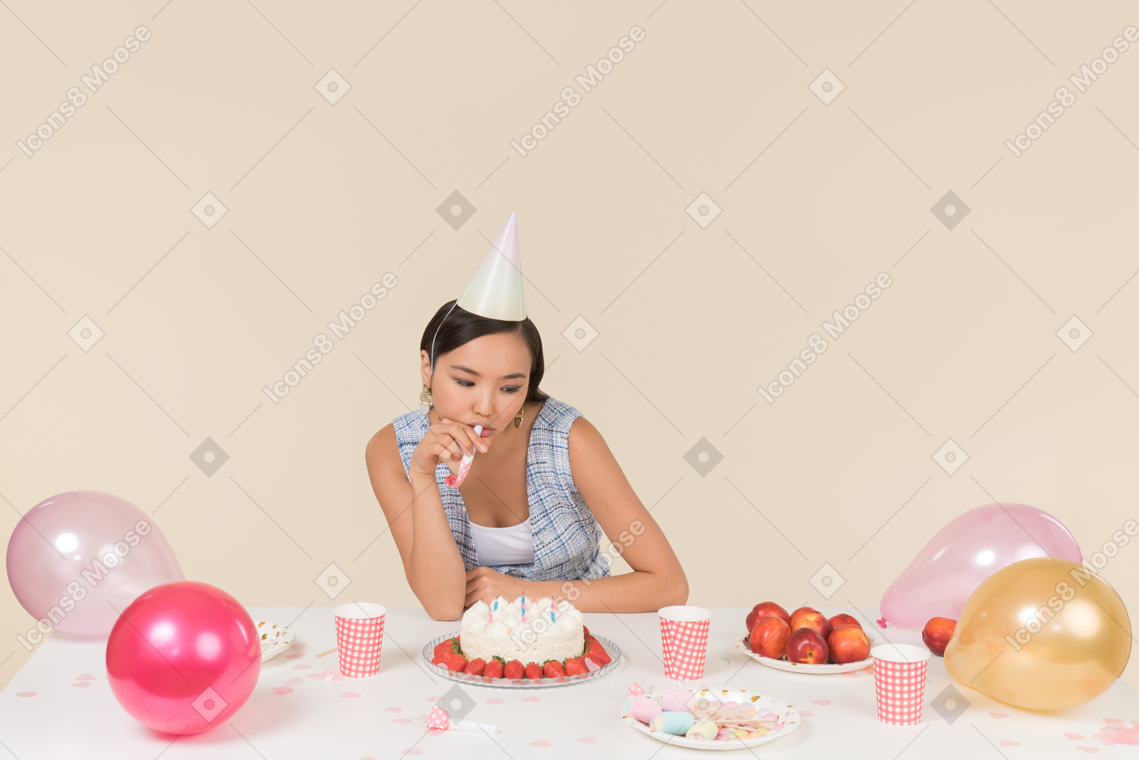 Jovem menina asiática sentado à mesa de aniversário e assobiando
