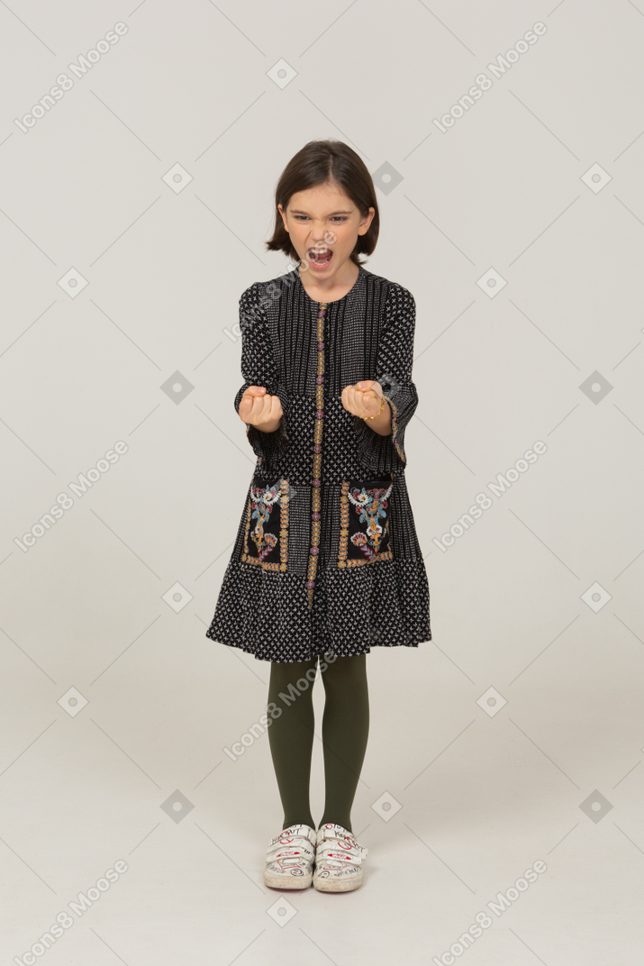 Front view of a furious little girl in dress clenching fists