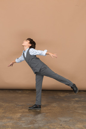 Вид сбоку на мальчика в костюме, балансирующего на одной ноге с вытянутыми руками