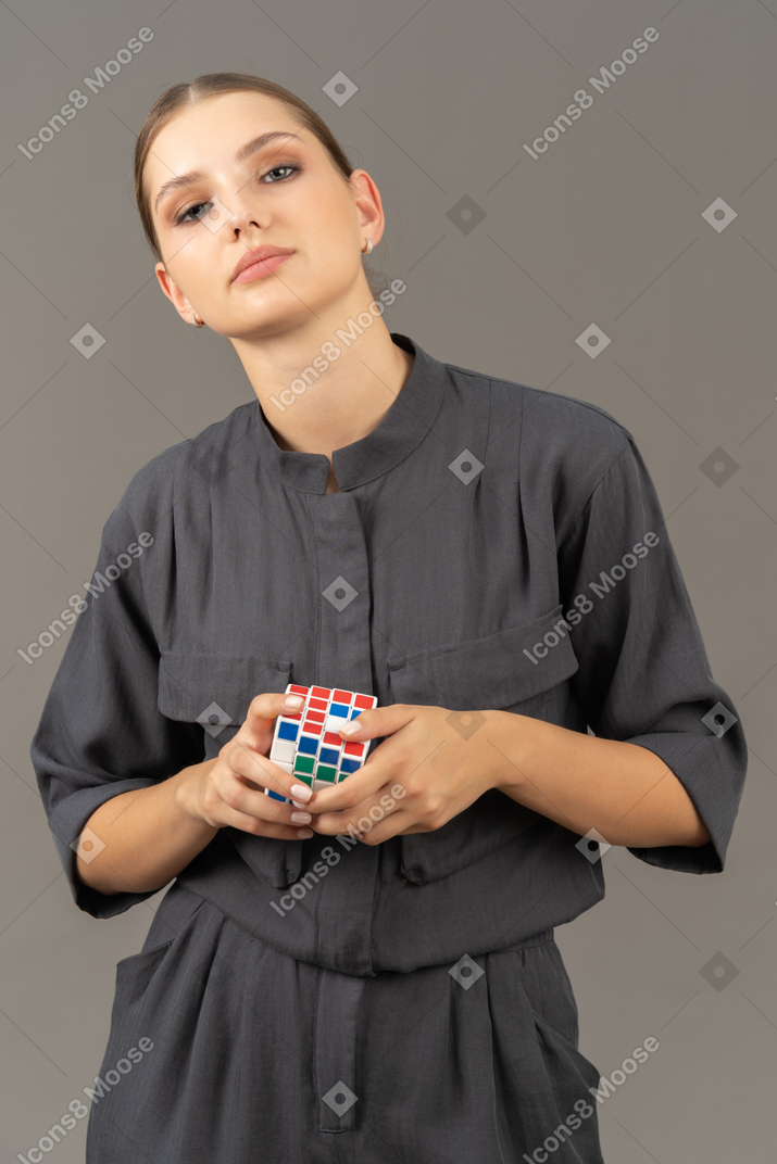 Vista frontal de uma jovem com um macacão segurando o cubo de rubik