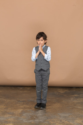 一个穿着灰色西装的男孩做祈祷手势的正面图