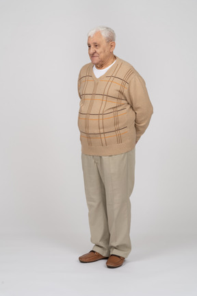 Front view of a happy old man in casual clothes standing with hands behing back
