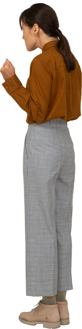Vista posteriore di tre quarti di una giovane donna asiatica gesticolante in calzoni e camicetta