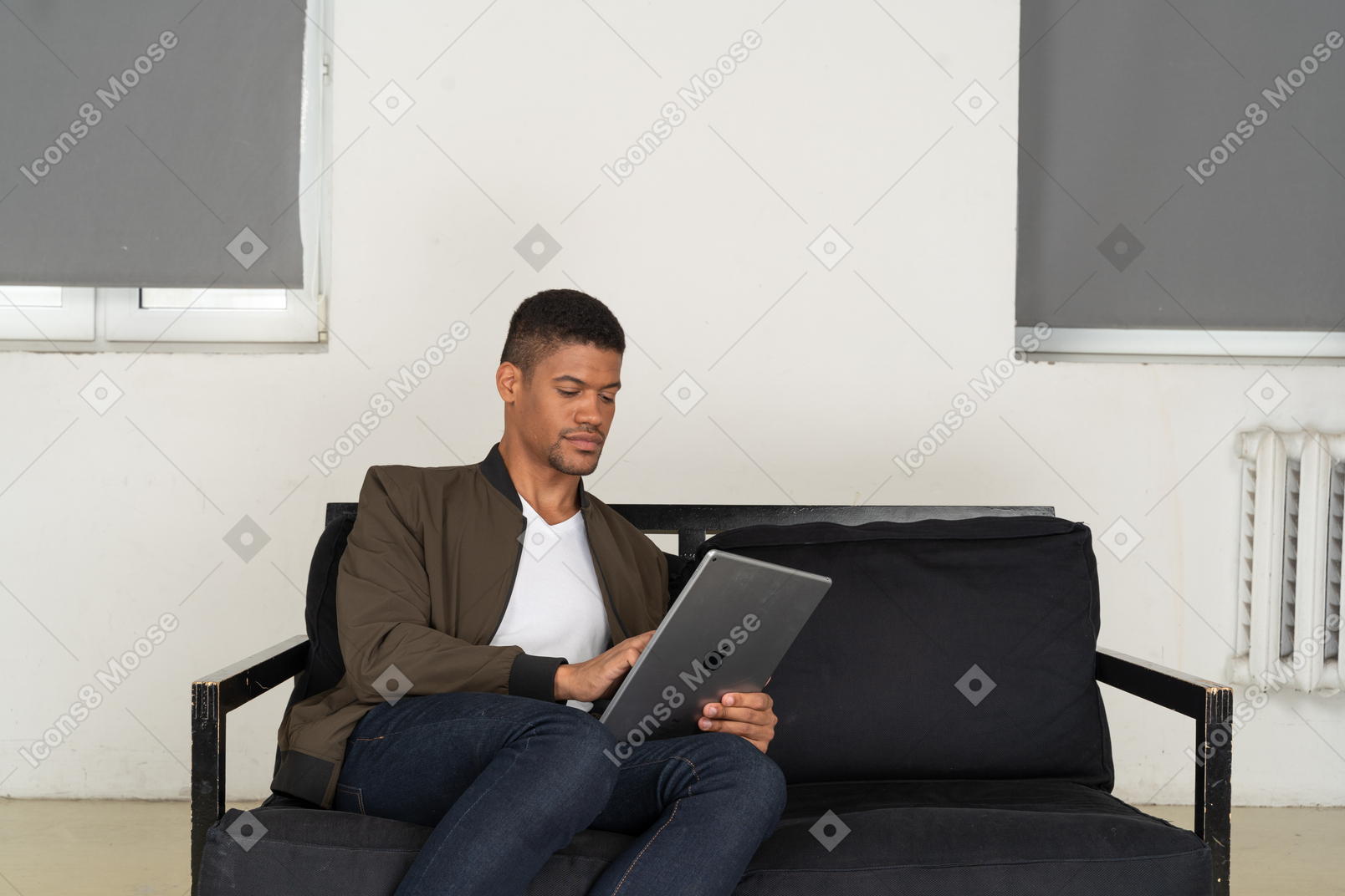 Front view of a bored young man sitting on a sofa while watching the tablet