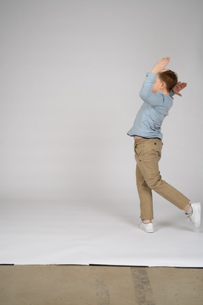 Side view of teenage boy running with his hands up