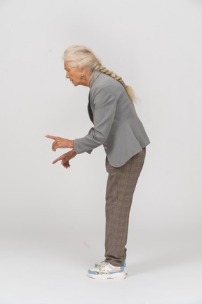 Вид сбоку на старуху в костюме, наклонившуюся и показывающую предупреждающий знак