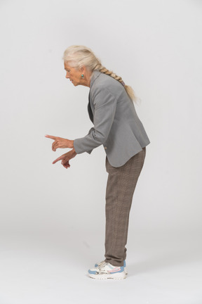 Side view of an old lady in suit bending down and showing warning sign