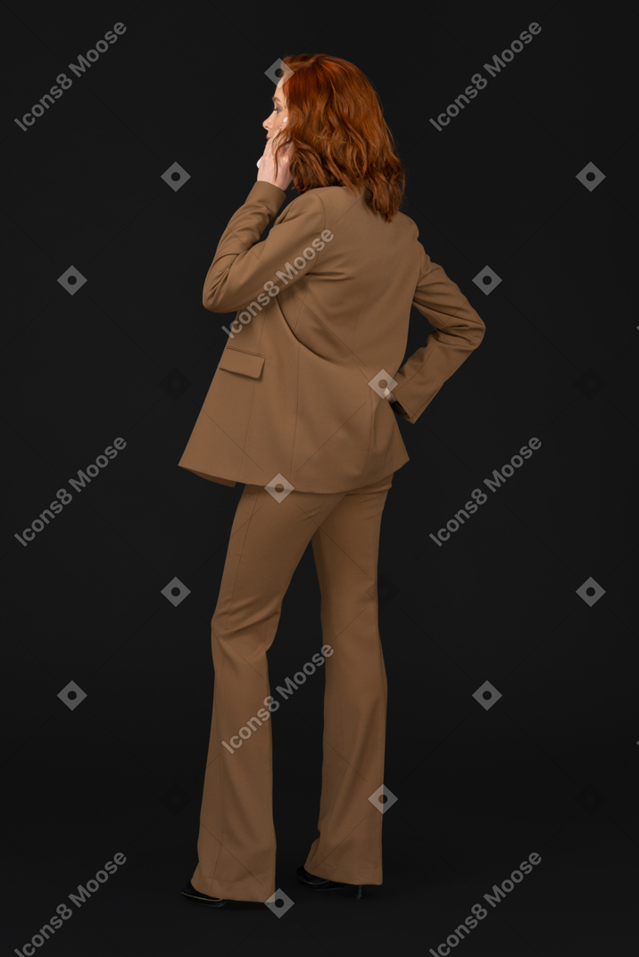 Standing half sideways back to camera young woman talking on the phone