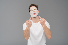 Front view of a young man in facial mask showing middle fingers