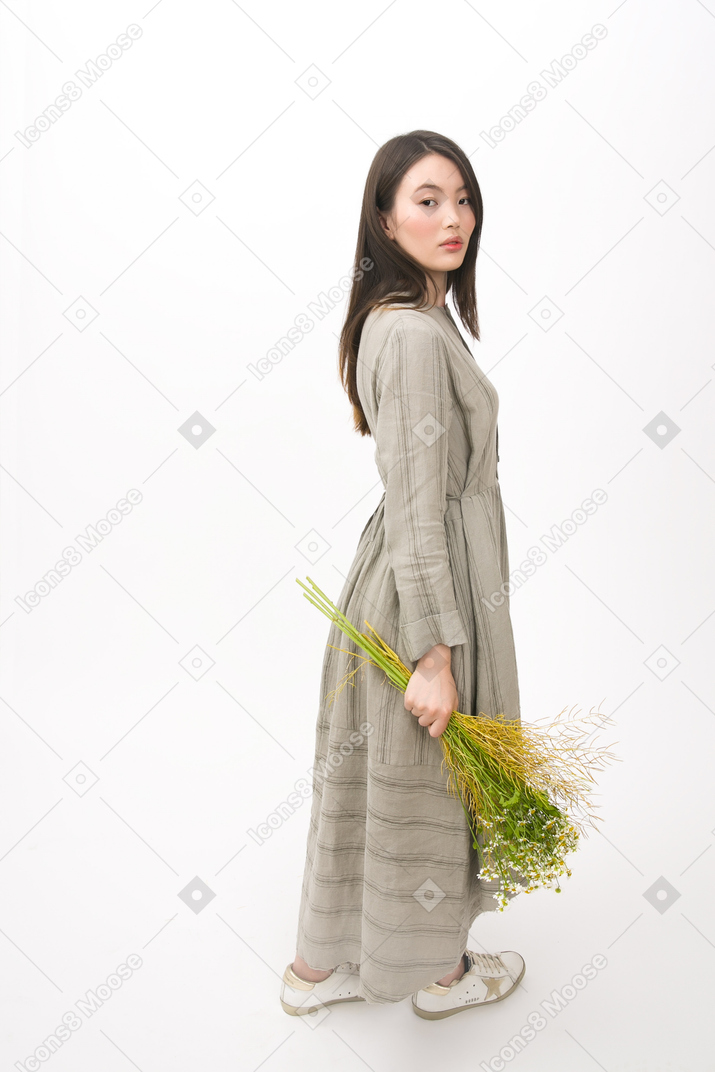 Girl holding a bouquet, standing halp aside and looking to the camera
