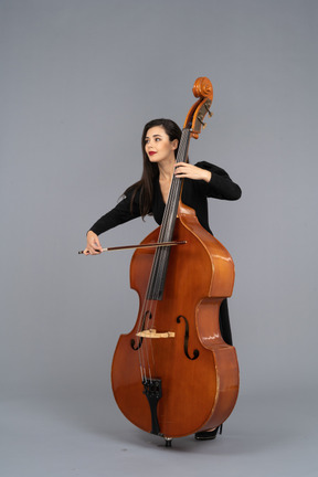 Vista di tre quarti di una giovane donna in abito nero che suona il contrabbasso con un arco