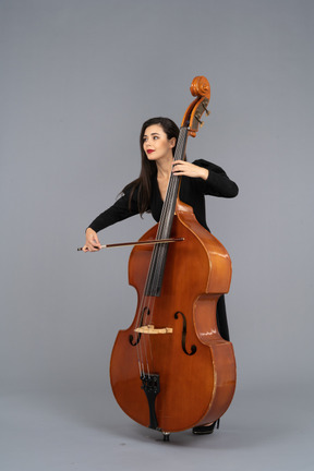 Three-quarter view of a young woman in black dress playing the double-bass with a bow