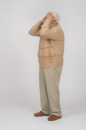 Vista lateral de un anciano con ropa informal que cubre los ojos con las manos