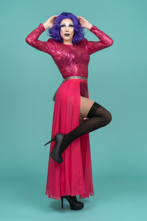 Porträt einer drag queen in rosa kleid, die ein bein hebt und den kopf mit beiden händen berührt