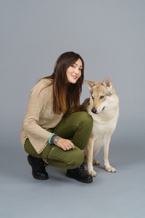 De cuerpo entero de una maestra sentada junto a su perro y mirando felizmente a la cámara