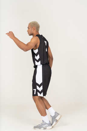 Vista lateral de un joven jugador de baloncesto masculino caminando levantando la mano
