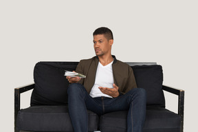 Front view of young man sitting on a sofa and passing pensil with notebook