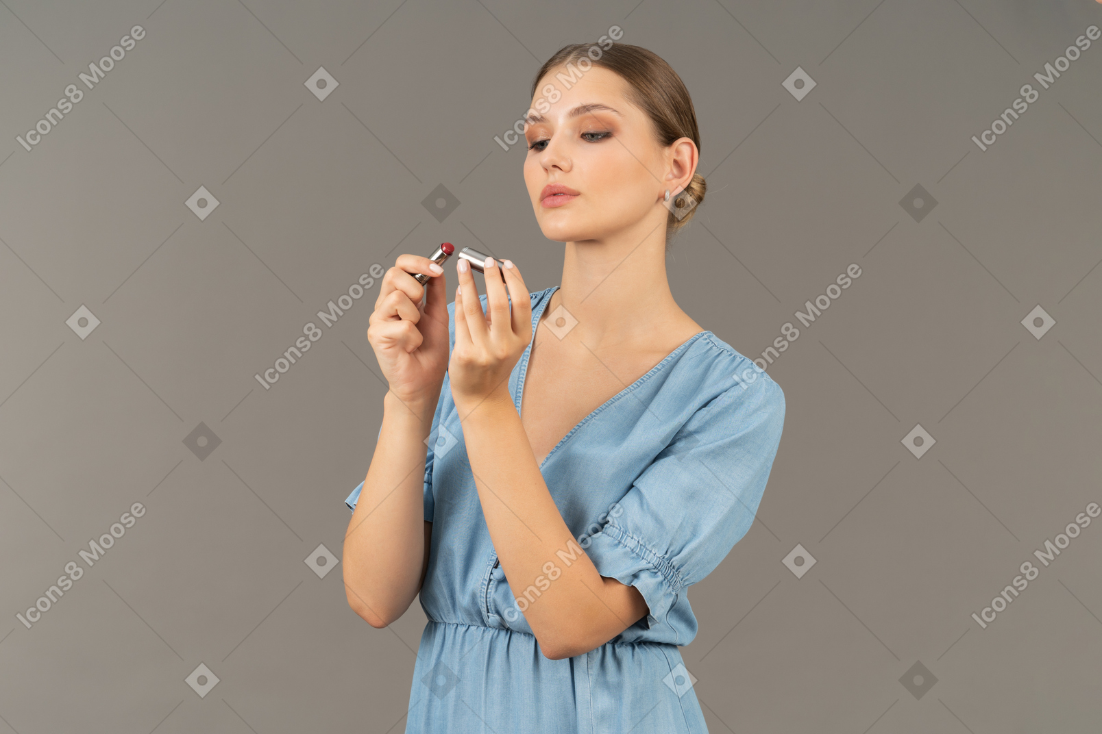 Three-quarter view of a young woman in blue dress opening lipstick