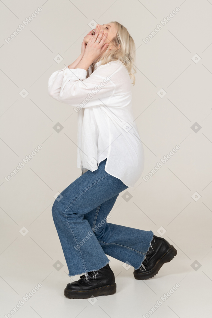 Side view of an exhausted blond female shouting and stepping aside while touching face