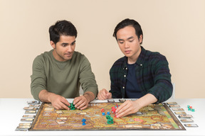 Interracial male friends sitting at the table and playing board game