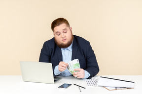 Jovem trabalhador de escritório com excesso de peso sentado na mesa e contando dinheiro
