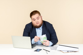 Young overweight office worker sitting at the desk and counting money