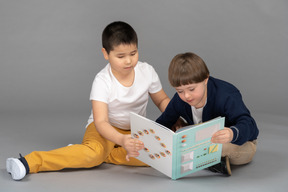 Two little friends sharing one colorful book