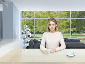 A pretty young woman in a beige sweater, drinking coffee in a bright modern living room, looking shy and unsure