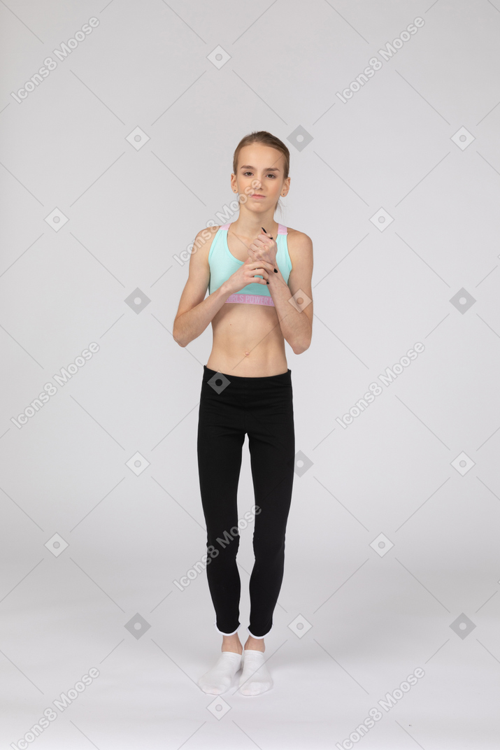 Vista frontal de uma adolescente perplexa em roupas esportivas tocando as mãos