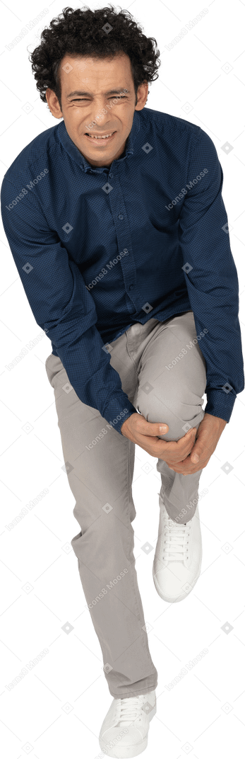 Front view of a man in casual clothes touching his hurting knee