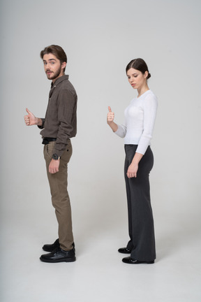 Side view of a cheerful young couple in office clothing showing thumb up