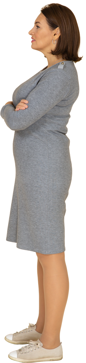 Vista laterale di una donna in abito grigio in piedi con le braccia incrociate