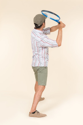 Young caucasian man holding tennis racket and standing back to camera